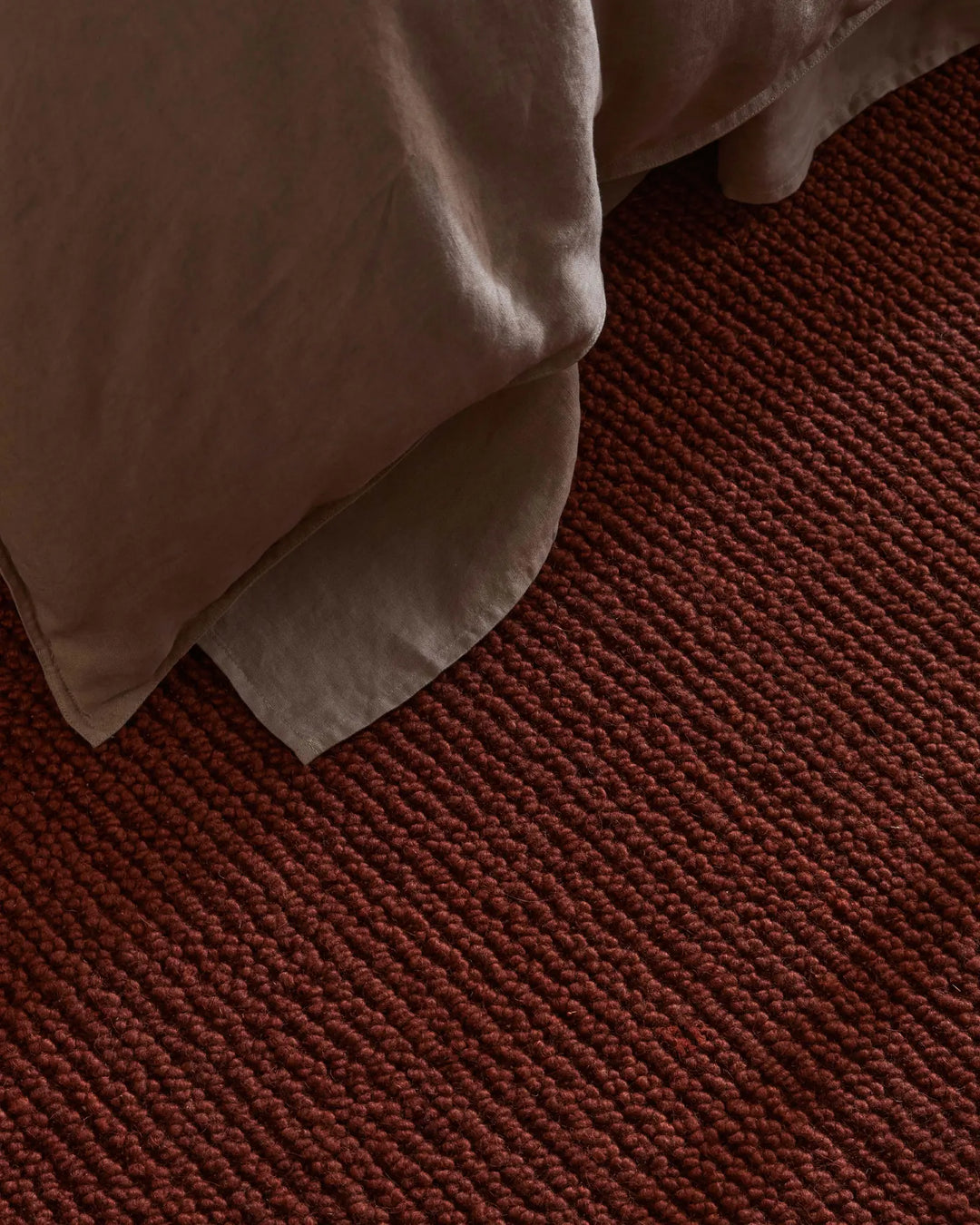 Neutral linen draped over deep rust wool rug, textural close-up showcasing warm terracotta palette and layered fabric weaves in minimalist interior styling