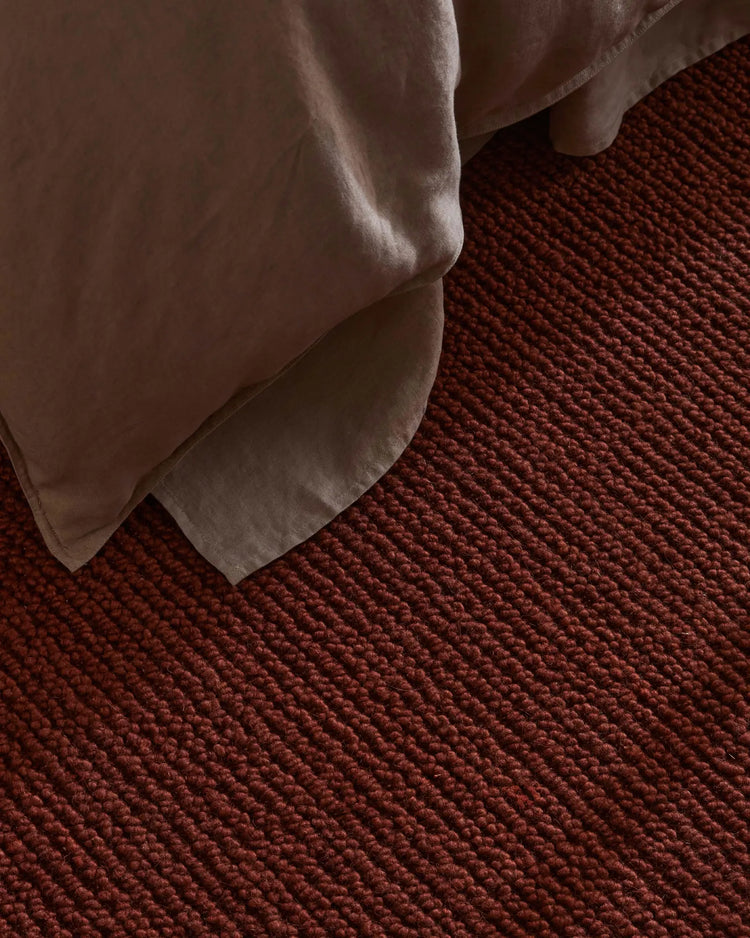 Neutral linen draped over deep rust wool rug, textural close-up showcasing warm terracotta palette and layered fabric weaves in minimalist interior styling