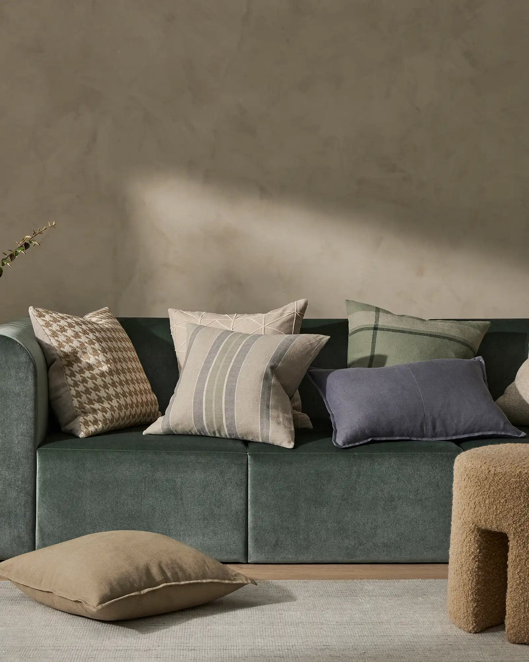 Neutral living room with sage green sofa styled with textured cushions in cream, taupe, and navy; Como Clay linen cushion in foreground, minimal aesthetic with soft natural light