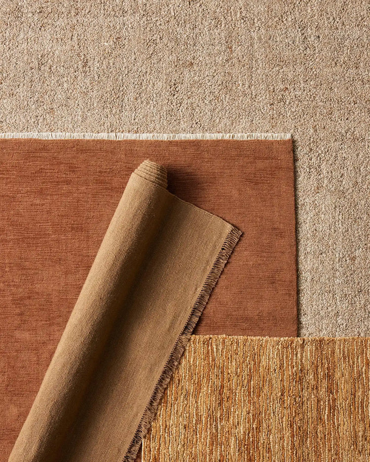 Layered rugs in warm earth tones: terracotta linen and natural jute textures create depth, showcasing neutral palette and woven material details