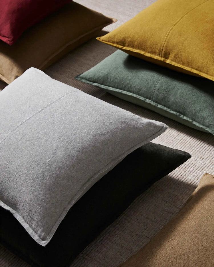 Linen cushions in muted earth tones—grey, sage, charcoal, ochre—arranged on neutral fabric, showcasing natural texture and minimalist interior styling