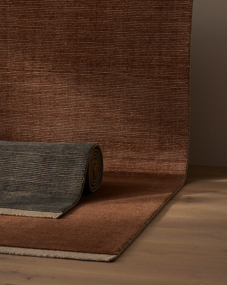 Remo rug in warm rust and sage tones layered on timber flooring, showcasing textured wool weave and neutral border detailing in earthy, minimalist interior styling