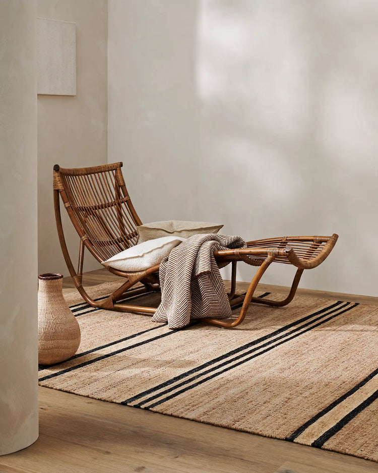 Minimalist room with natural jute rug, woven rattan lounge chair, cream linen cushions, and herringbone throw in neutral tones with black striping