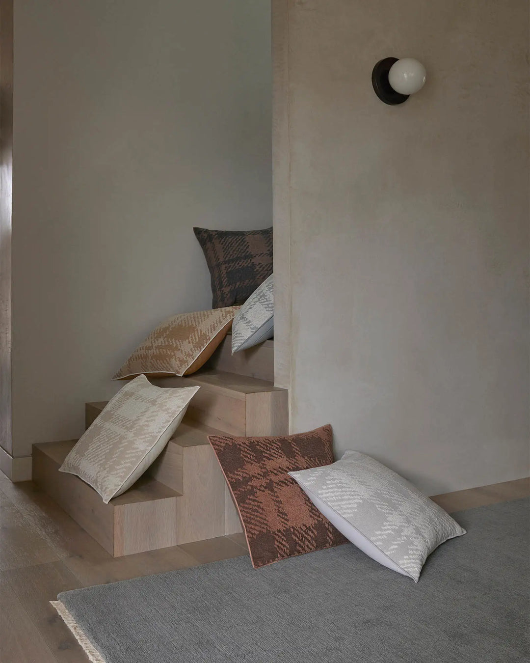 Neutral minimalist room styled with Sienne cushions in warm earth, cool grey, and natural tones arranged on blonde wood blocks against soft white and beige walls