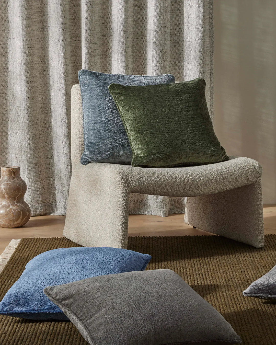 Neutral living room with cream curved chair, striped linen curtains, and Tempo cushions in forest green and marine blue on textured olive rug