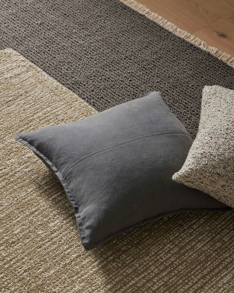 Neutral layered living space styled with charcoal linen cushion, cream and grey wool rugs, and warm timber flooring in earthy tones