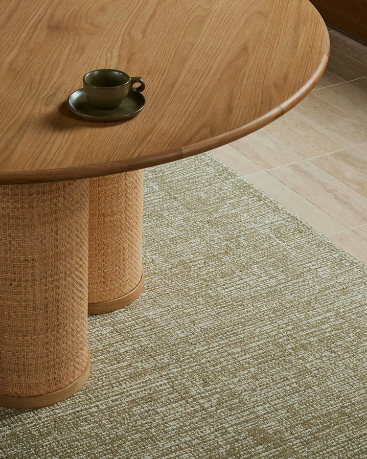 Warm timber dining table and rattan base with Kaia Willow wool rug in sage green, paired with olive ceramic tableware in minimalist Scandinavian interior