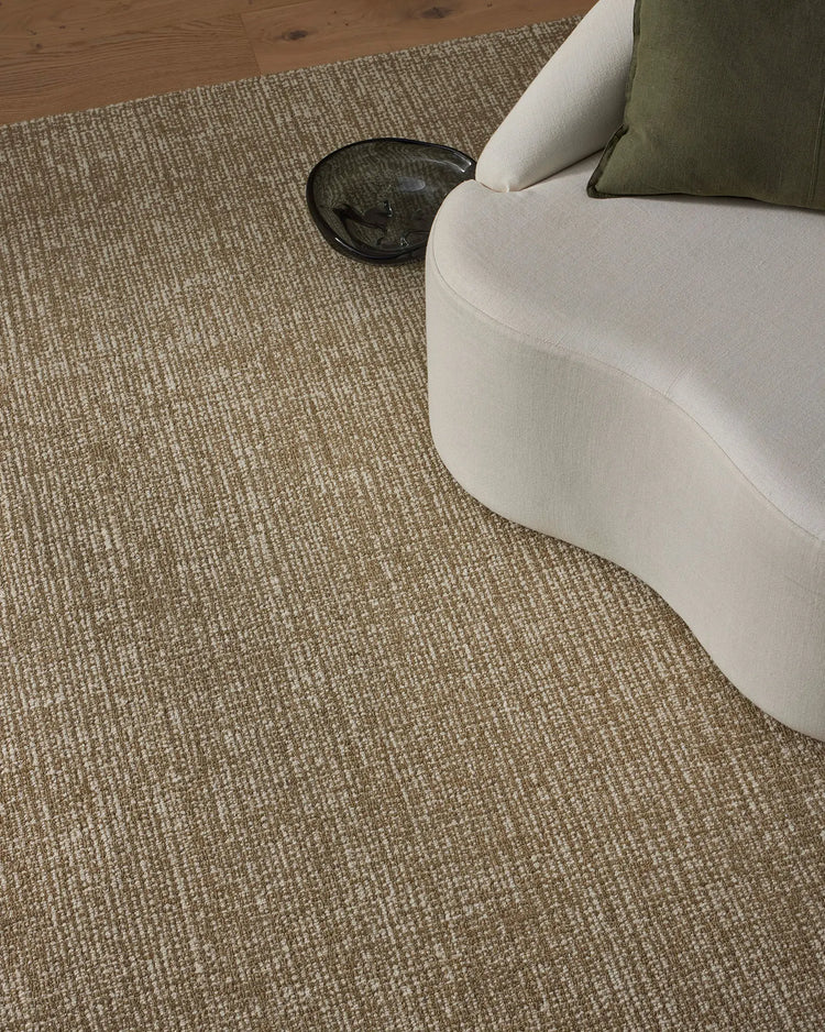 Neutral living room styled with Kaia Willow high-traffic rug in warm beige wool, cream armchair, olive cushion, and natural wood flooring for contemporary comfort