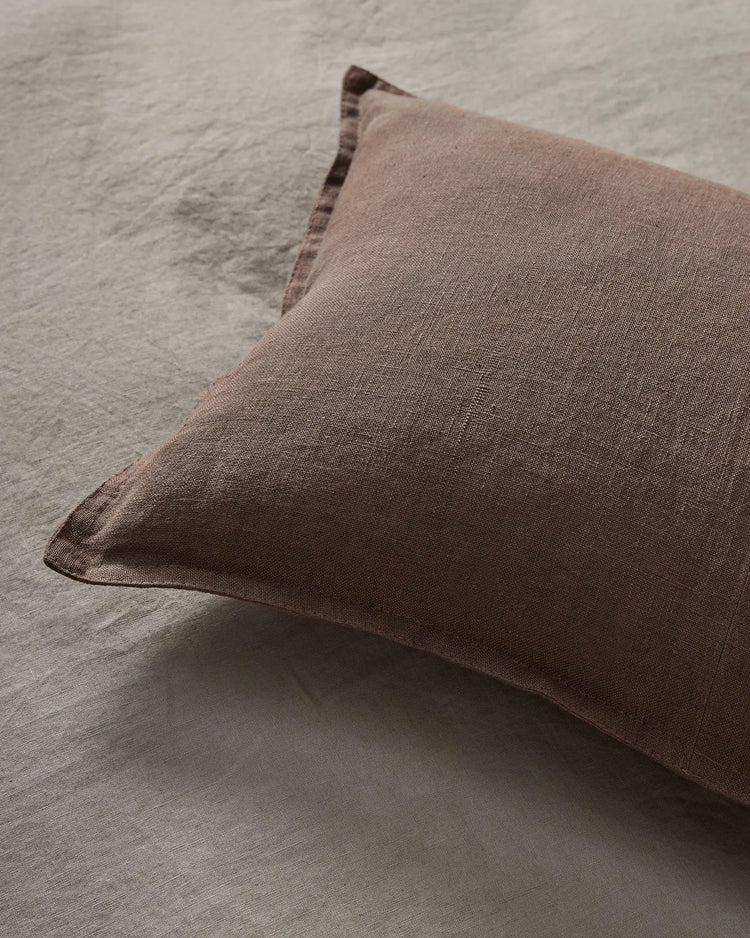Mocha linen cushion resting on neutral textured bedding, showcasing warm earthy tones and natural fabric textures in minimalist bedroom styling