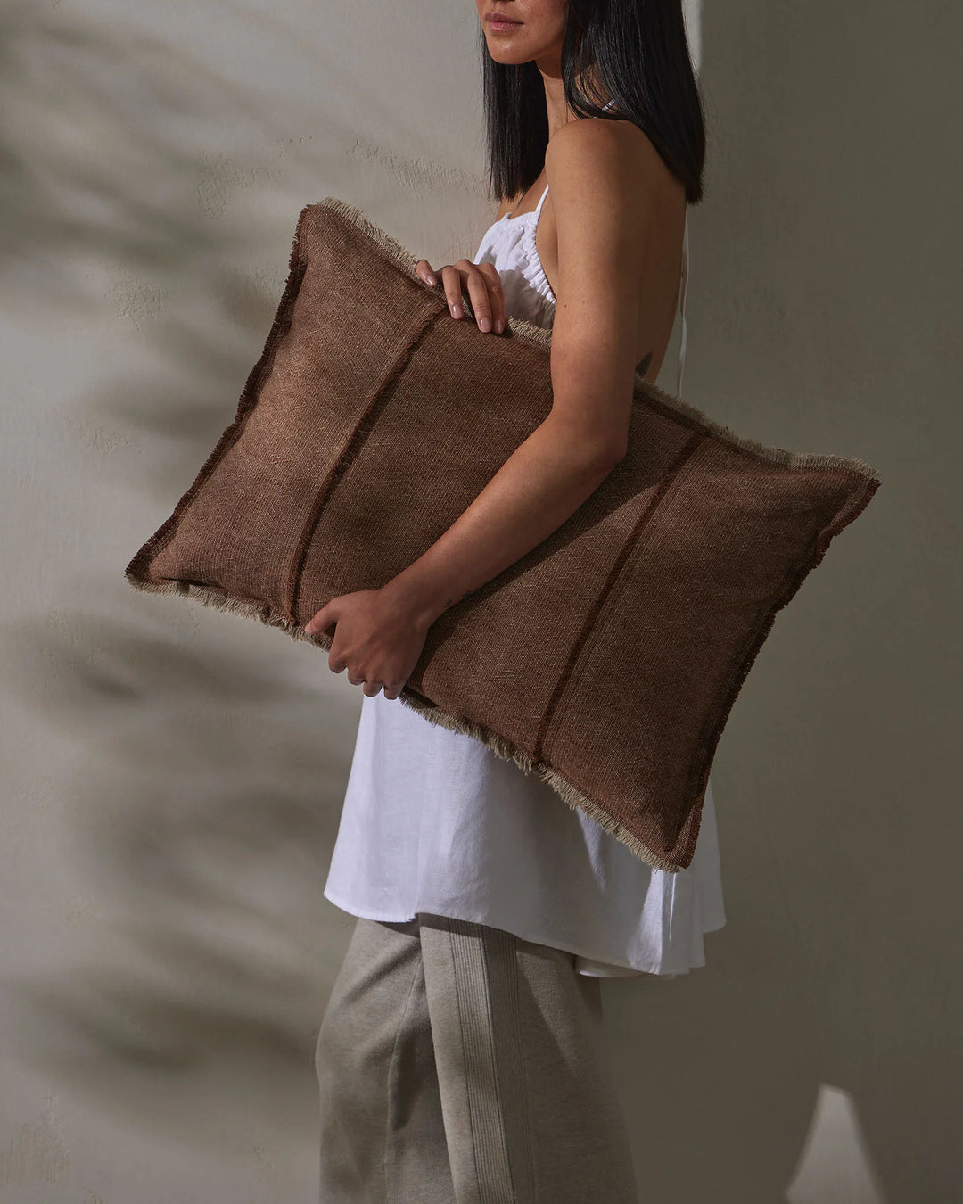 Warm rust cushions with frayed edges styled in neutral minimalist setting with white and beige linens, earthy colour palette