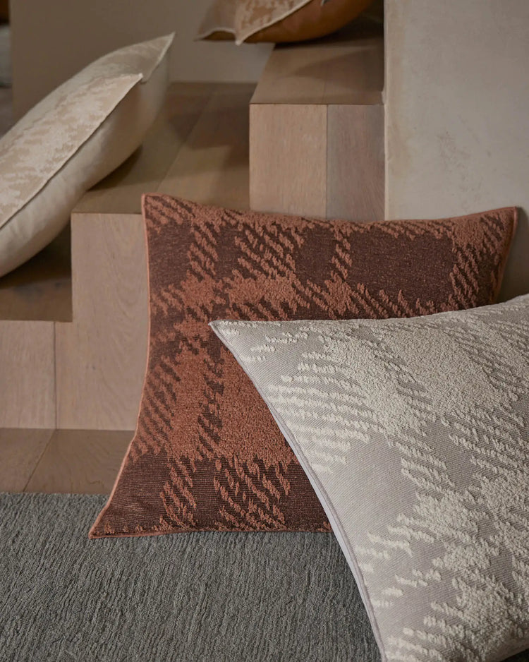 Neutral bedroom styling with Sienne Earth and Moonbeam cushions featuring geometric jacquard textures in warm terracotta and cream tones, layered against soft grey bedding and natural wood furniture