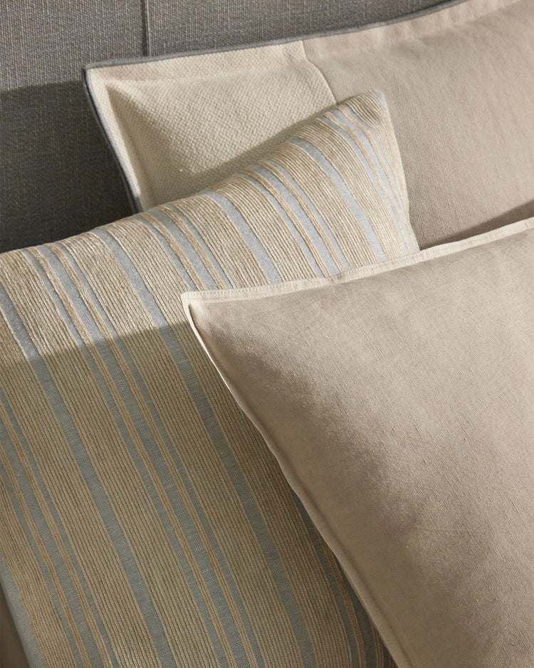 Neutral linen cushions with subtle striped patterns in sage and warm tones layered on a cream upholstered sofa, showcasing textural home décor styling