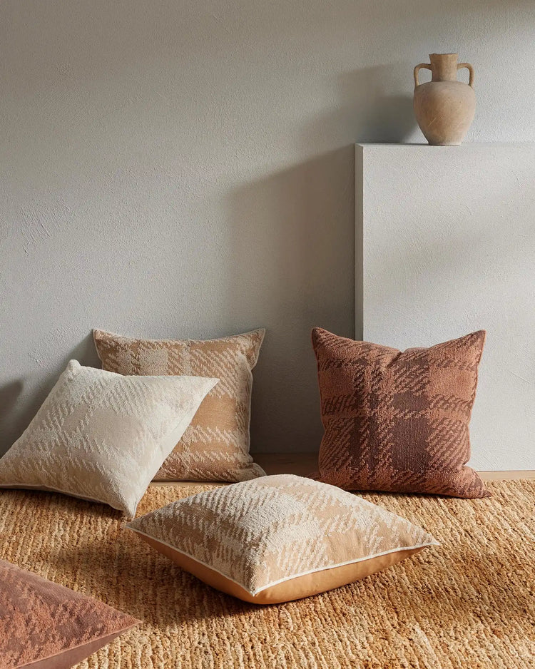 Warm terracotta and natural beige textured cushions styled on a jute rug with white plaster pedestal, embodying earthy minimalist interior design