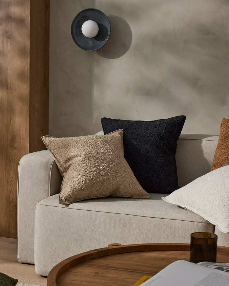 Neutral living room with cream curved sofa styled with textured cushions in charcoal and warm taupe tones, warm wood accents and minimalist décor