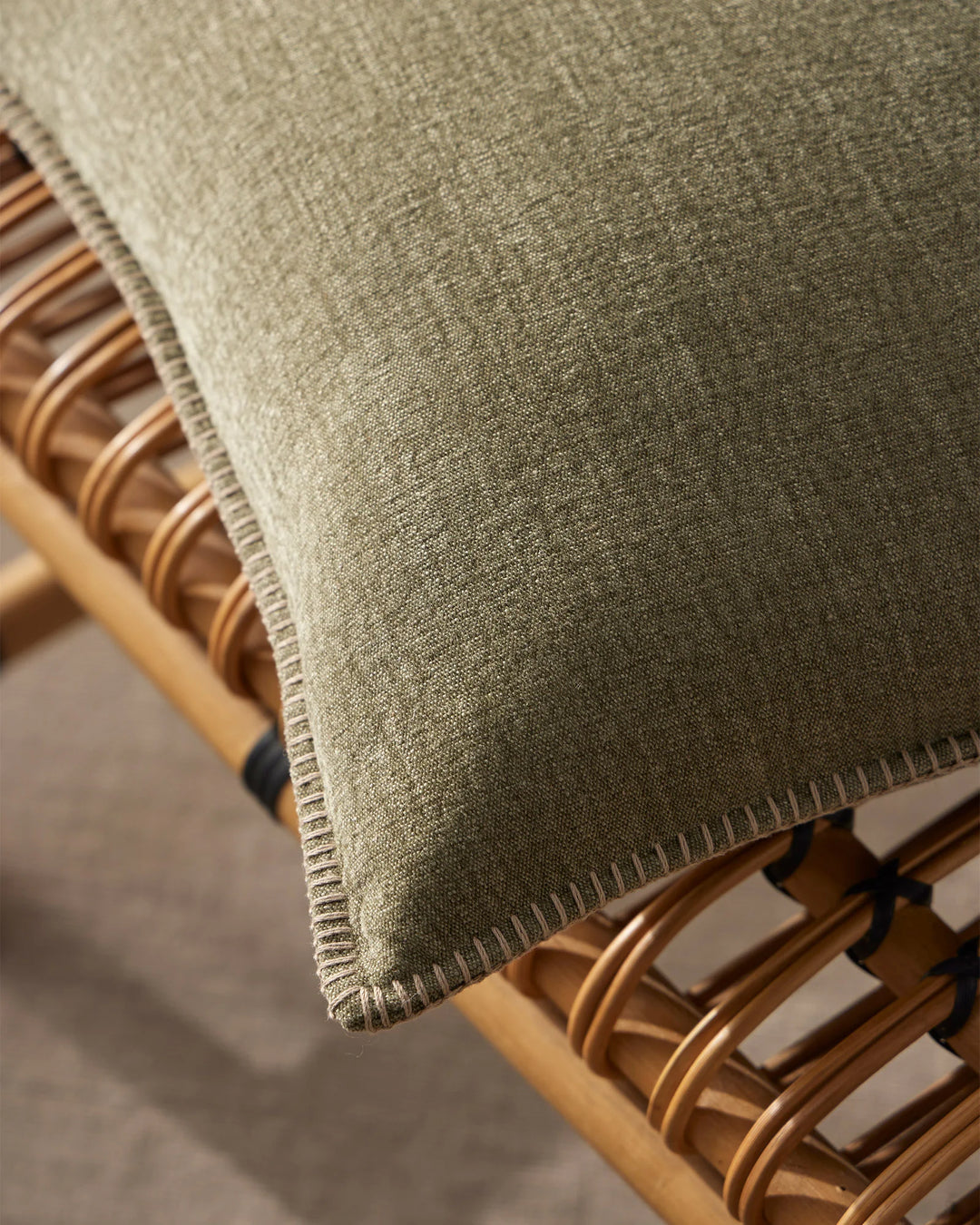 Sage green linen cushion with blanket stitch edge detail draped over timber chair with woven rattan details, natural textile styling