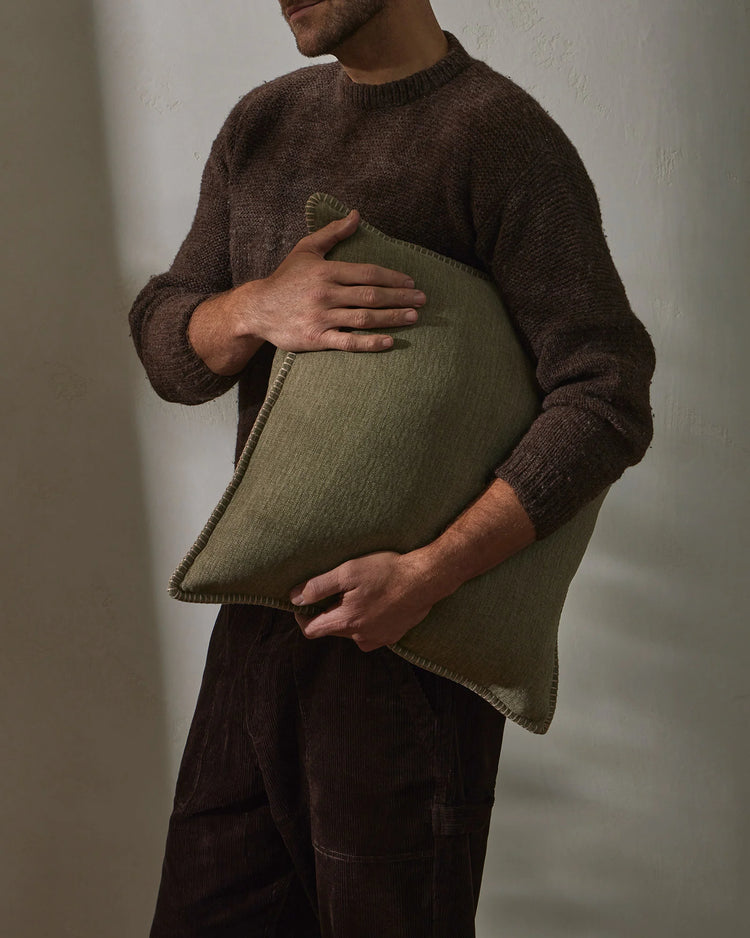 Earthy-toned lifestyle scene with sage-green Alba cushion paired with warm brown knit, textured linen weave and neutral palette styling