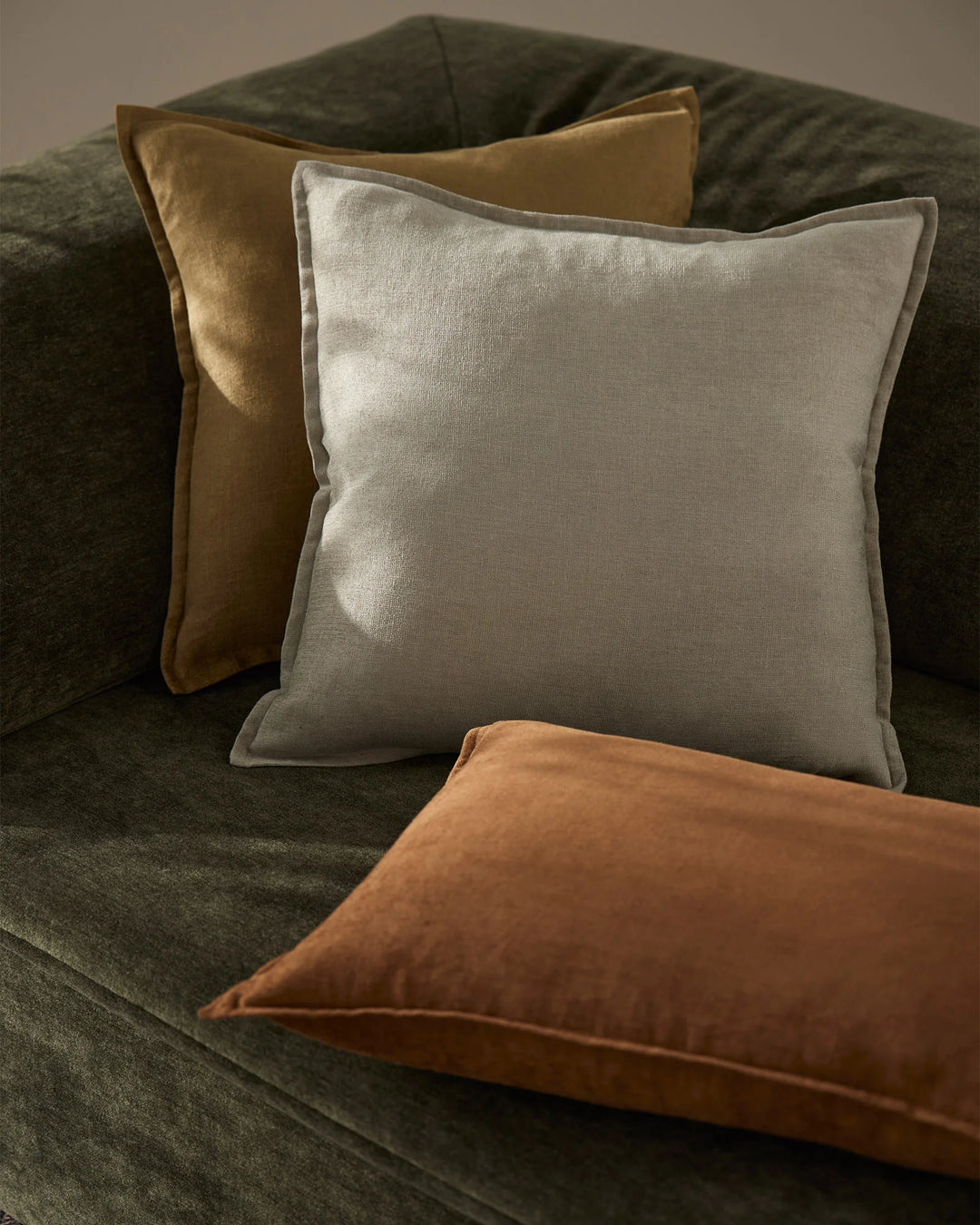 Neutral linen cushion styled with sage and ochre tones on a charcoal upholstered sofa, earthy colour palette with textured fabric layers and modern interior styling