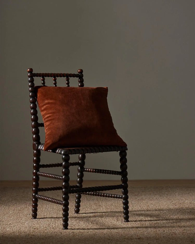 Rust-toned Ava cushion on dark wood spindle chair with natural beige rug, warm earthy palette, vintage farmhouse styling