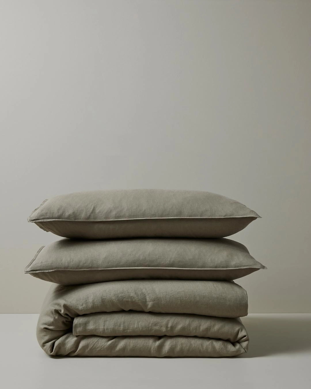 Stacked neutral linen bedding in sage-grey tones: Ravello Pillowcases and Quilt Cover arranged to showcase soft linen texture and minimalist bedroom styling