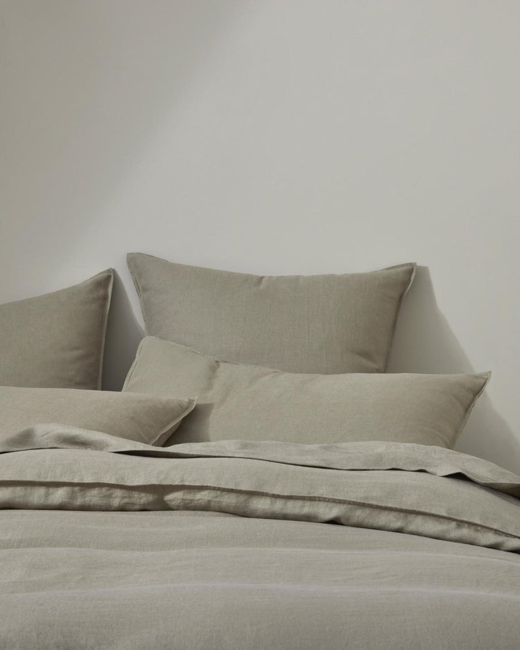 Neutral linen bedding styled on bed with layered pillows and quilt cover in warm sand tones, showcasing natural linen texture and minimalist bedroom aesthetic