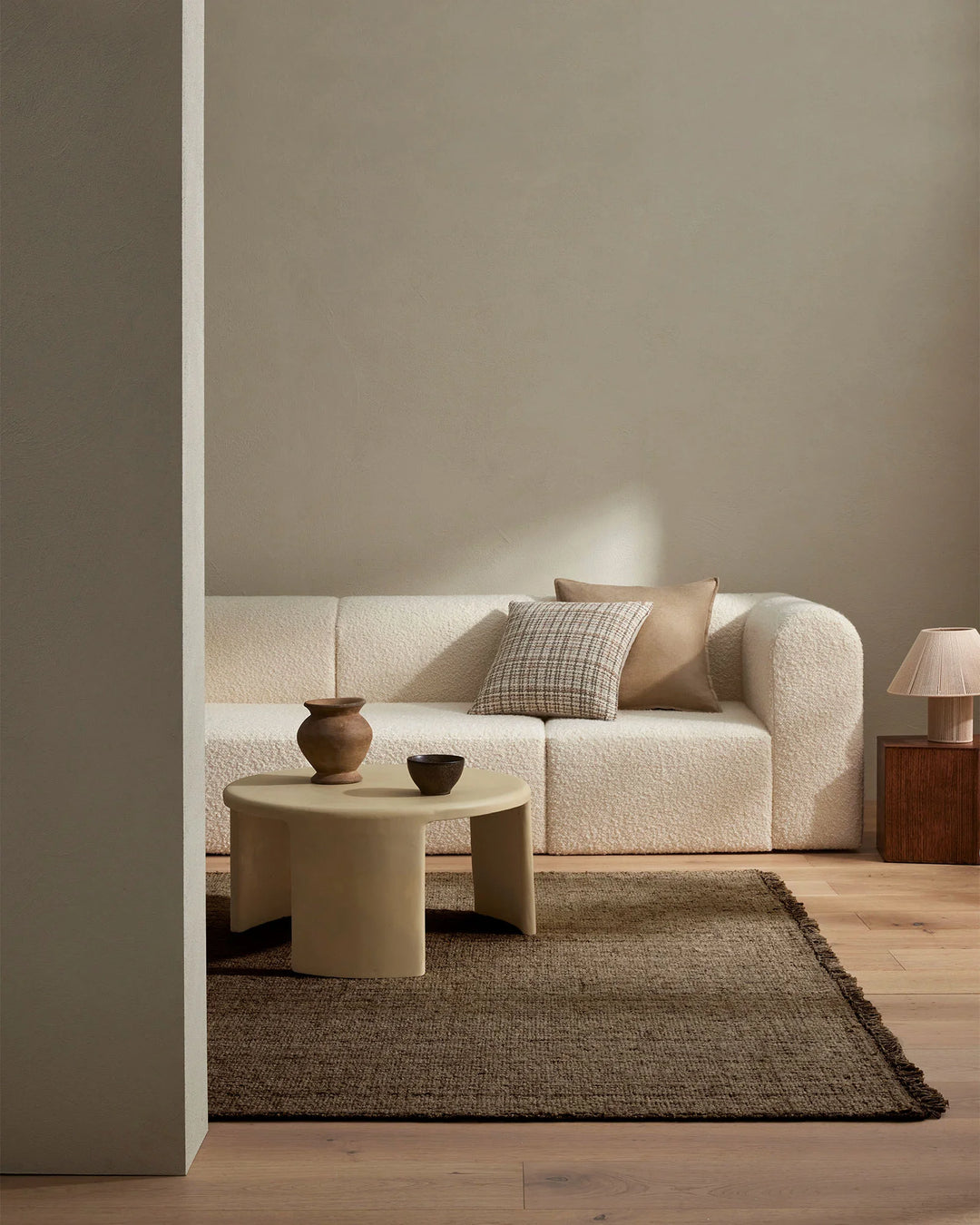 Minimalist living room with cream boucle sofa, neutral earth-tone palette, textured Puglia rug anchoring the space, and warm natural light casting soft shadows on taupe walls