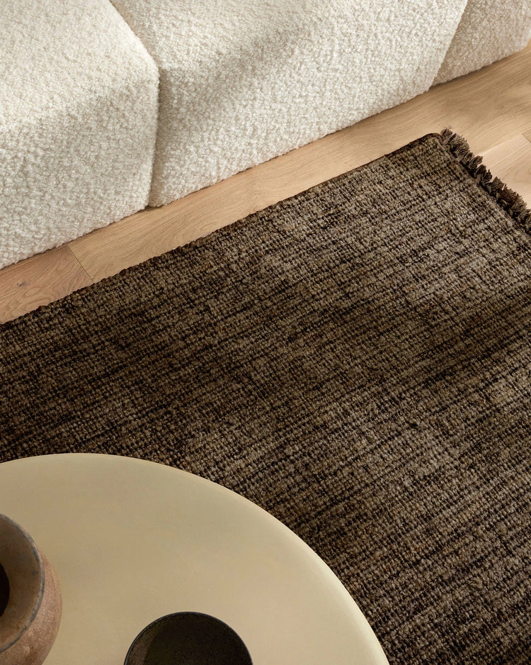 Neutral living room with cream boucle armchair, warm oak flooring, and charcoal wool-blend Puglia rug layered for earthy, textured appeal