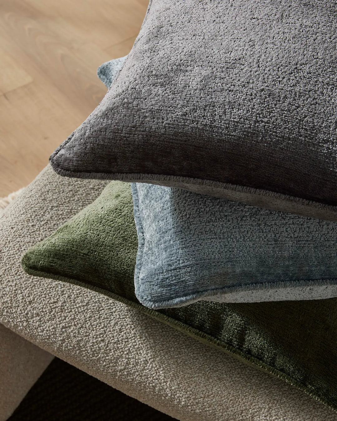 Stacked Tempo cushions in charcoal, sky blue and forest green on a neutral linen chair, showcasing layered texture and contemporary colour blocking