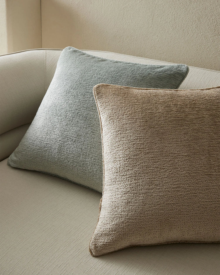 Neutral minimalist living room with textured Tempo cushions in sage green and natural beige layered on a cream upholstered sofa against soft taupe walls