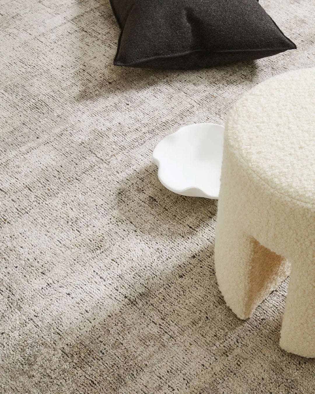 Neutral minimalist interior with cream and charcoal textiles layered on textured beige rug, showcasing soft furnishings and muted earthy tones