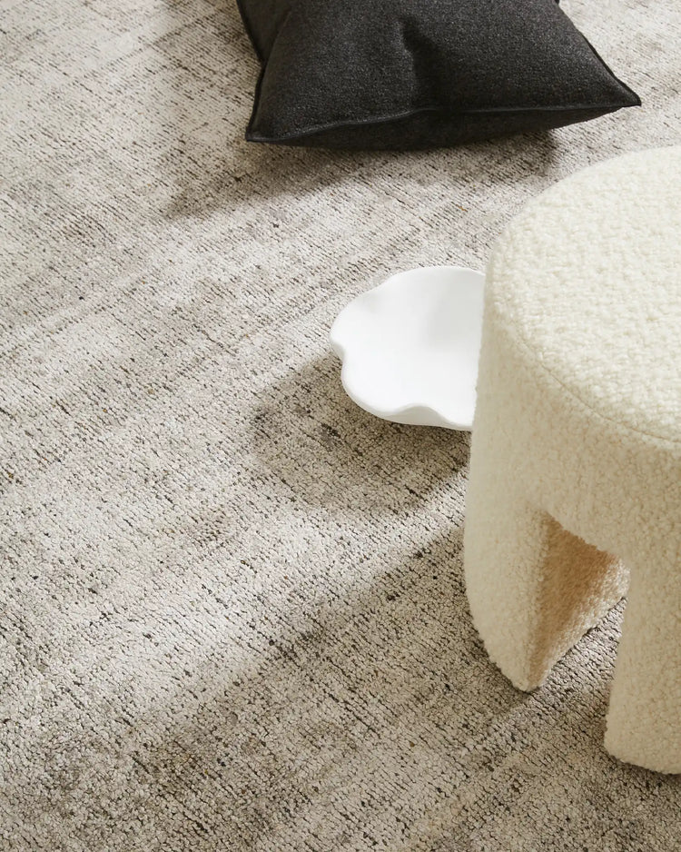 Neutral minimalist interior with cream and charcoal textiles layered on textured beige rug, showcasing soft furnishings and muted earthy tones