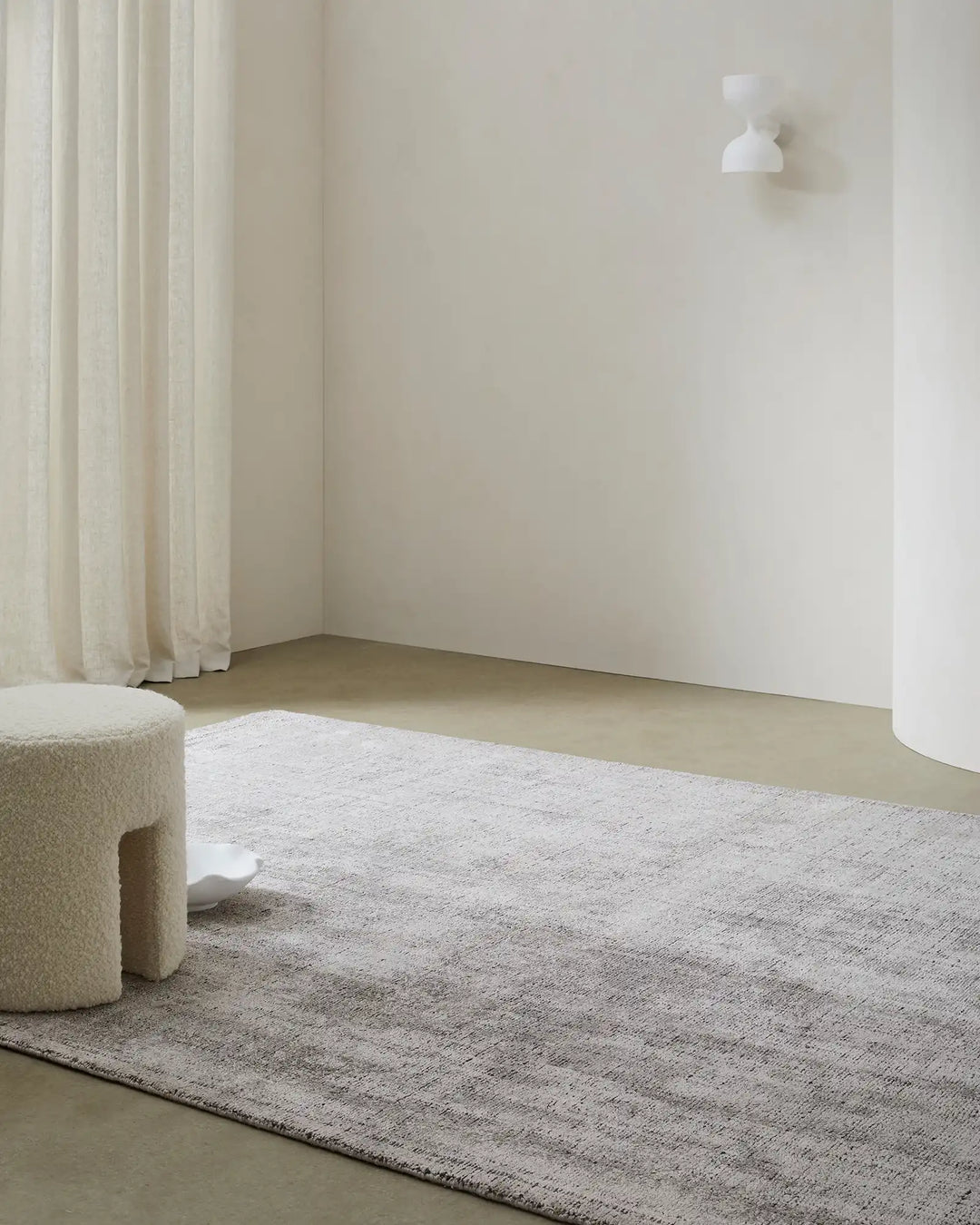 Minimalist room with Matisse Shale low-traffic rug in neutral beige tones, cream linen curtains, textured poufs, and soft natural light creating a calm, understated aesthetic
