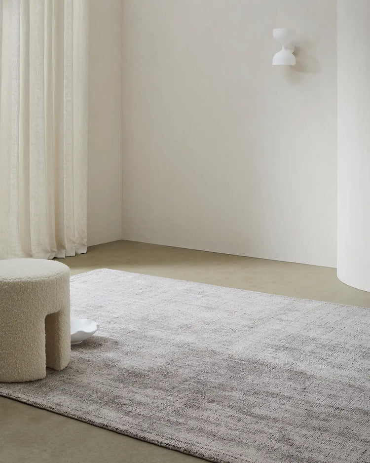 Minimalist room with Matisse Shale low-traffic rug in neutral beige tones, cream linen curtains, textured poufs, and soft natural light creating a calm, understated aesthetic