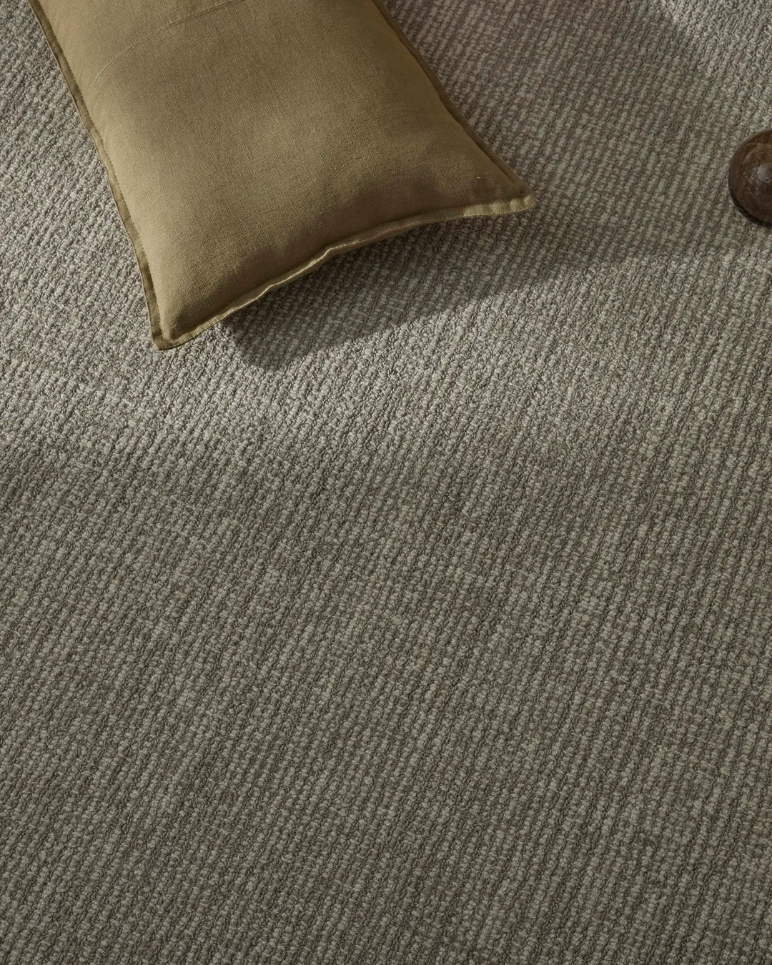 Neutral wool rug in textured weave with ribbed pattern, styled with sage linen cushion for soft, earthy living space aesthetic