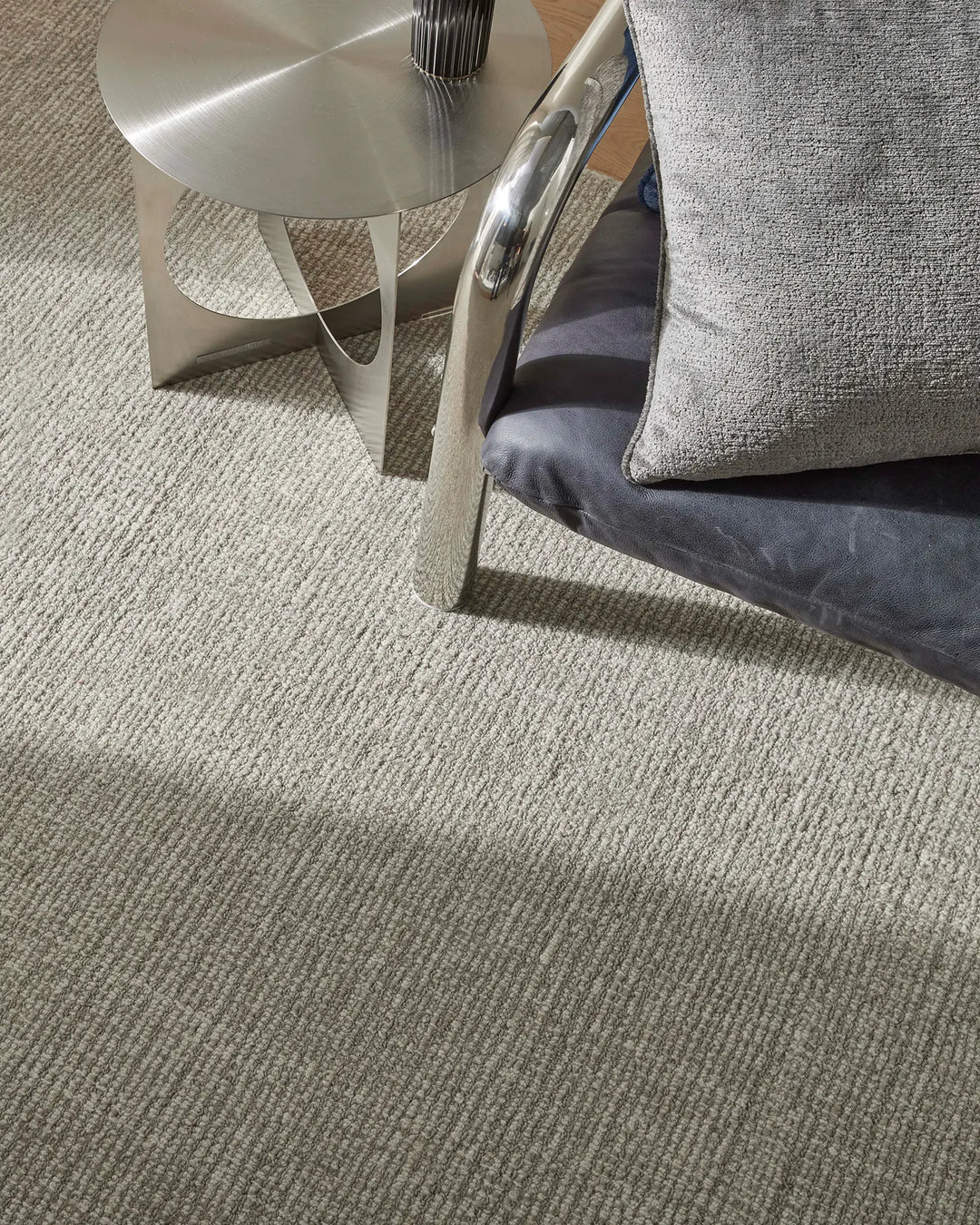 Neutral wool rug with ribbed texture in minimalist living room styled with chrome side table and grey upholstered seating