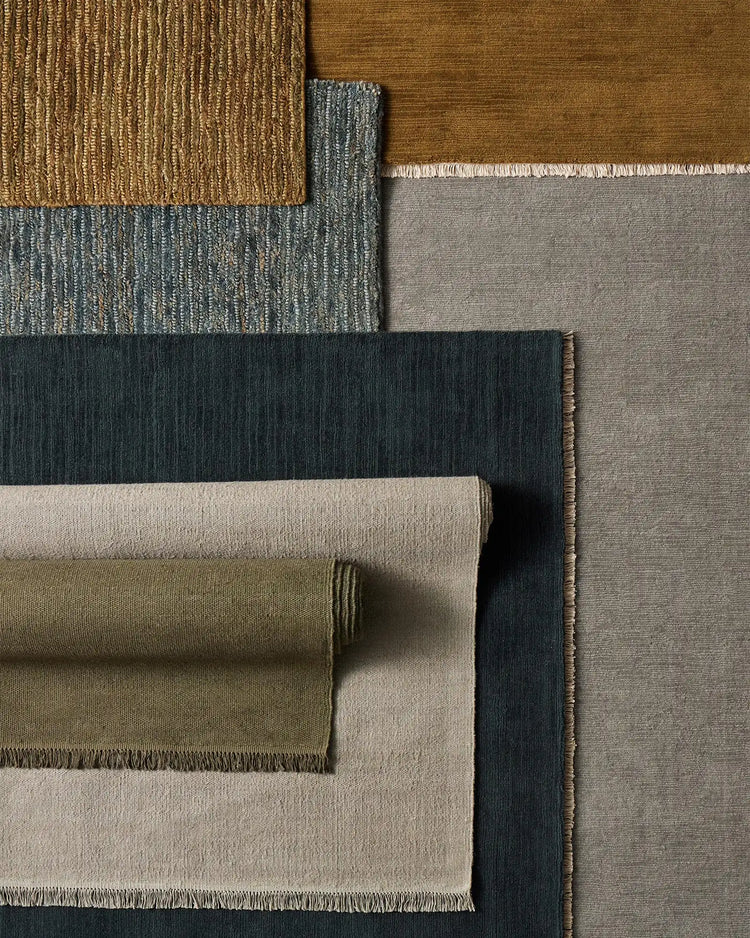 Layered neutral and earth-tone rugs in jute and wool showcase textural variety, from warm ochre and sage to cool charcoal and soft grey with woven and flat weave finishes