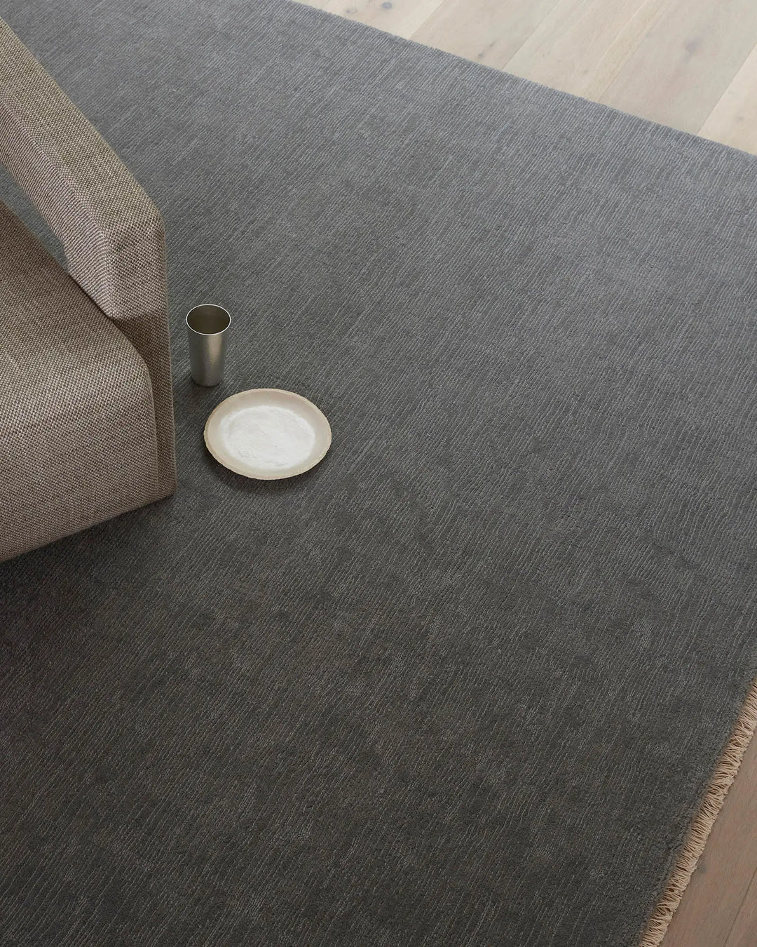Charcoal wool rug with natural texture anchors minimalist styling, paired with neutral upholstered seating and ceramic accents on light timber floor