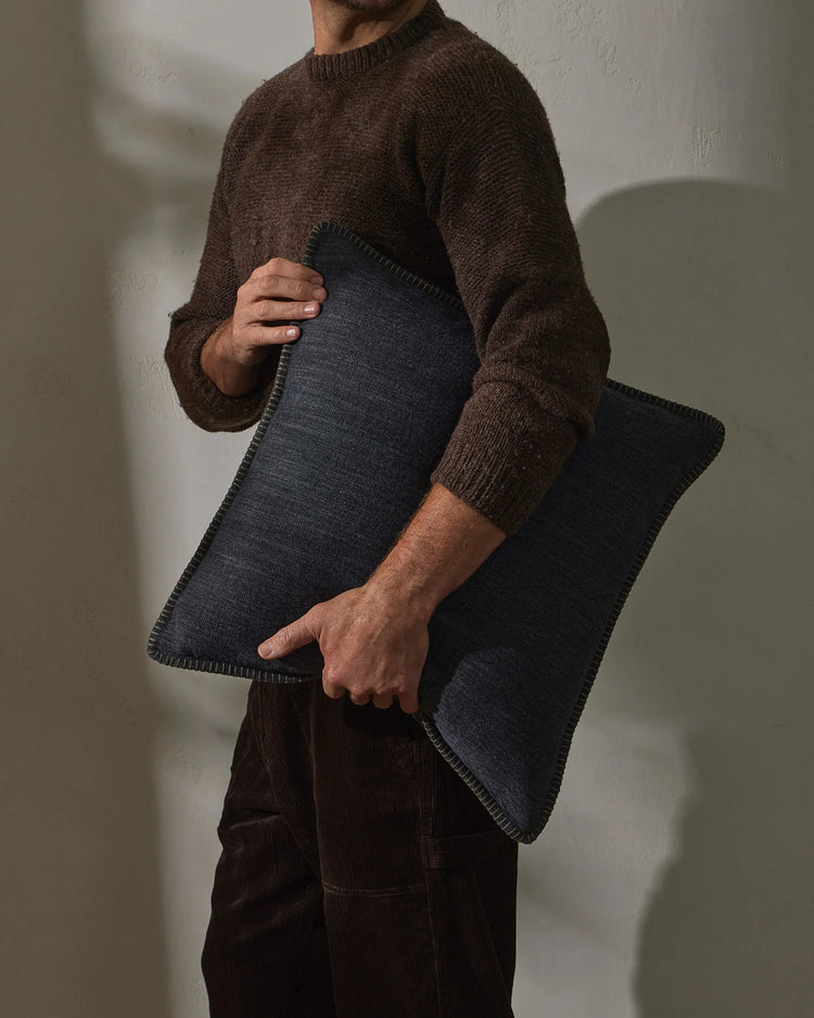 Man holding charcoal linen cushion against brown knit sweater, earthy colour palette with natural textures, minimalist styling against white backdrop