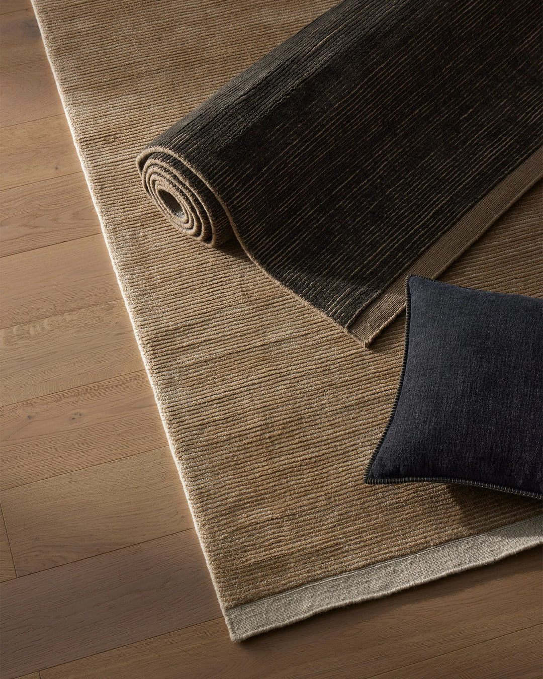 Neutral and charcoal wool rugs layered on warm timber flooring with an ocean blue linen cushion, showcasing textured weaves and earthy tones in a minimalist interior styling.