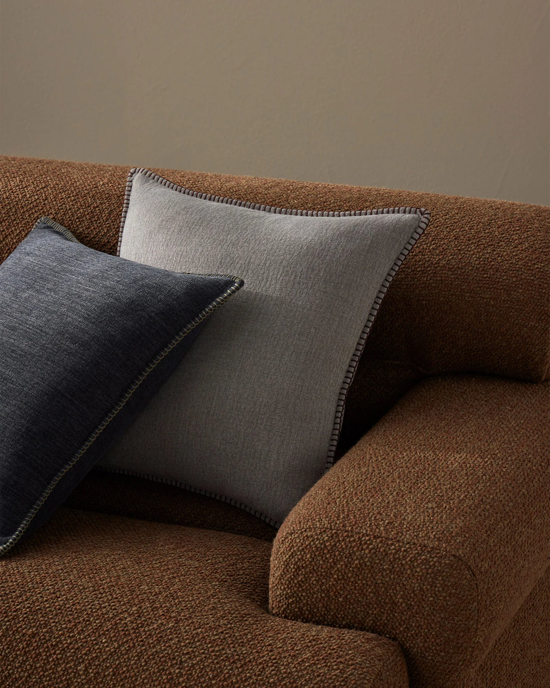 Warm terracotta armchair styled with Alba cushions in dove grey and ocean blue, featuring contrast blanket stitching and natural linen textures