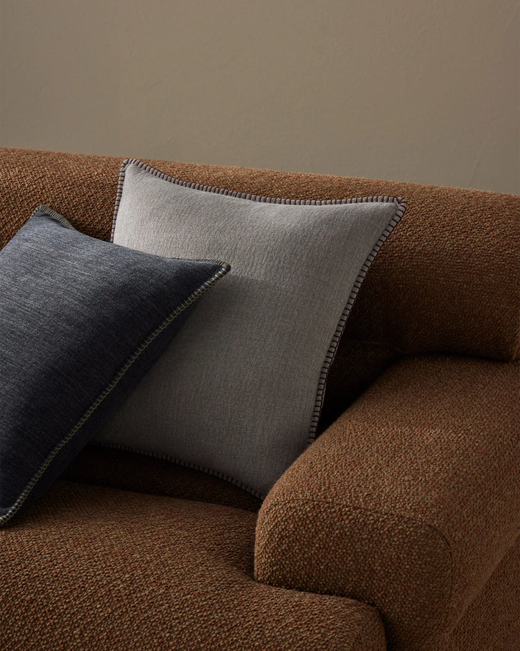 Warm terracotta armchair styled with Alba cushions in dove grey and ocean blue, featuring contrast blanket stitching and natural linen textures