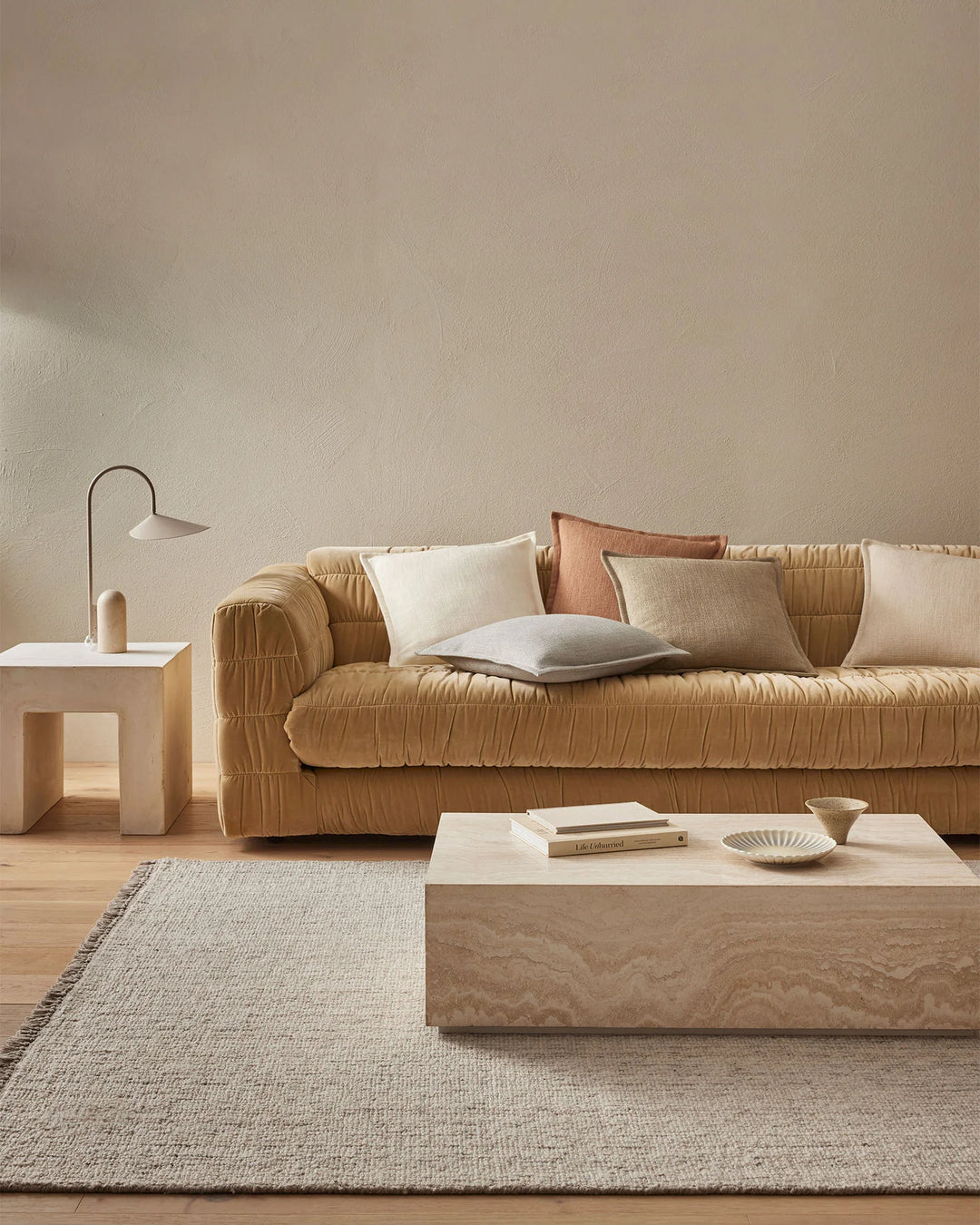 Minimalist living room with caramel quilted sofa layered with Figlio cushions in cream, sage and terracotta tones, natural wood coffee table, linen rug and neutral palette throughout