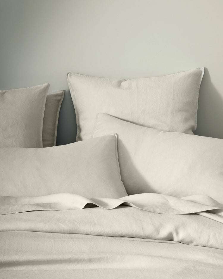 Neutral linen bedding styled flat lay with Ravello quilt cover, flat sheet and pillowcases in bone, showcasing soft European linen texture and relaxed, undone aesthetic