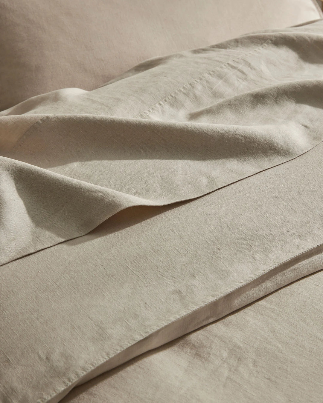 Close-up of layered natural linen bedding in cream, showing soft folds and texture of European linen sheets with tactile, relaxed styling