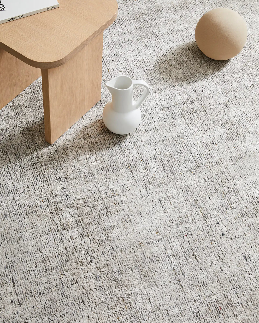 Minimalist interior with light oak furniture and white ceramic pitcher on neutral Matisse rug, textured weave in soft greys and creams