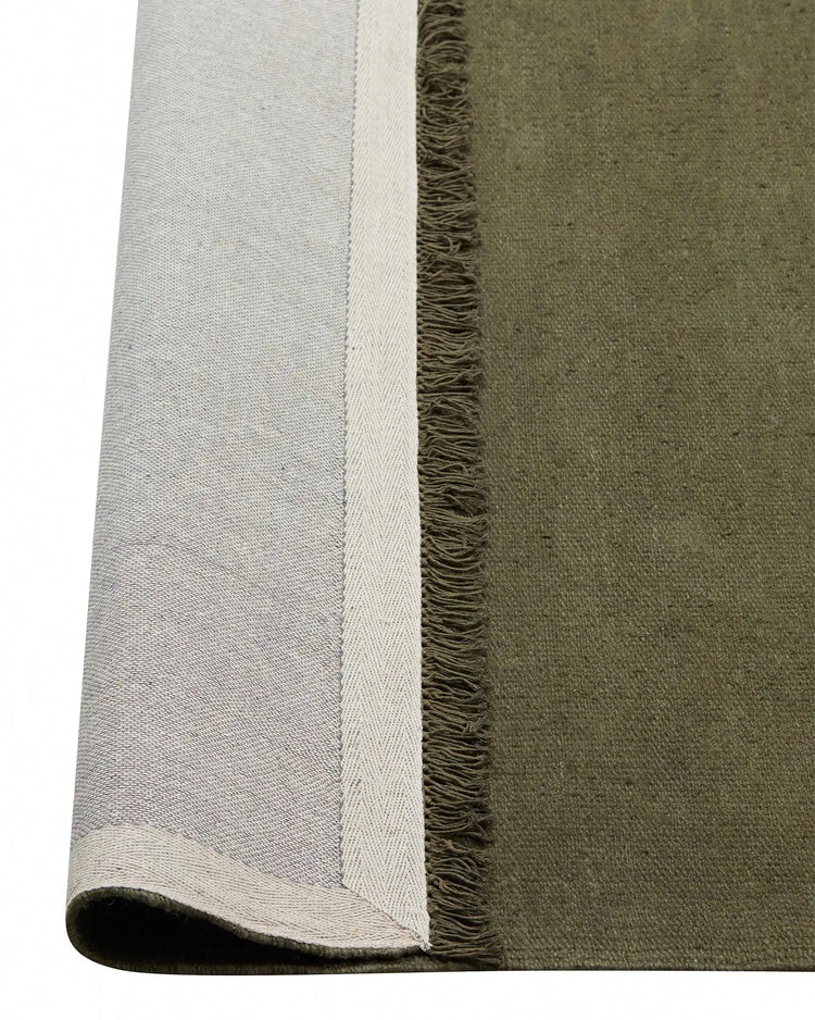 Emilio Kale linen rug detail showing deep forest green weave with cream fringe border, flat-weave construction by Weave Home