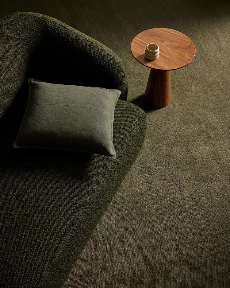 Sage green linen rug in modern living room with olive cushion on curved chair, warm wood side table, and natural light creating soft shadows