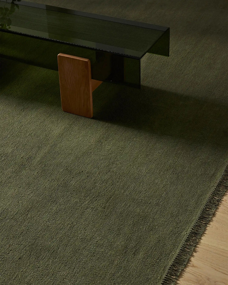 Sage green linen rug in modern minimalist interior with wooden chair and black desk, showcasing textured weave and fringed edge detailing.