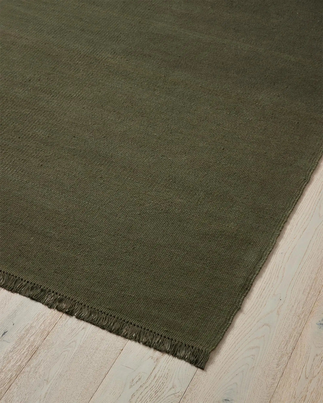 Emilio Kale linen rug corner detail, showing deep forest green flat-weave with fringe edge, 2m x 3m by Weave Home