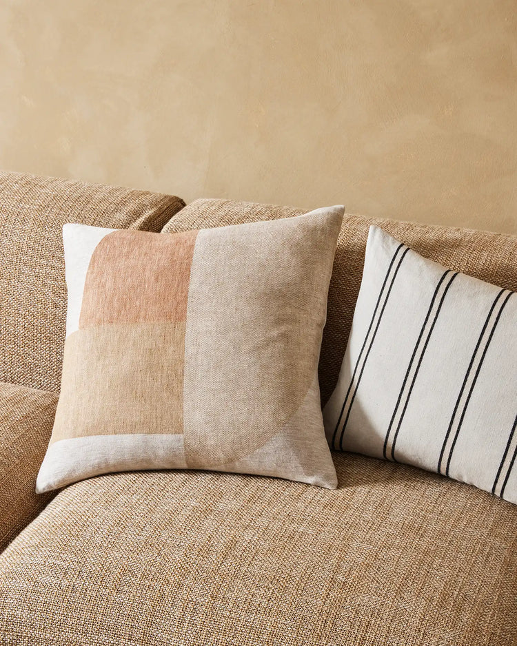 Neutral linen sofa styled with geometric colour-block and striped cushions in warm sand, cream and charcoal tones, layered with a textured throw for a minimalist, Scandinavian-inspired living room aesthetic