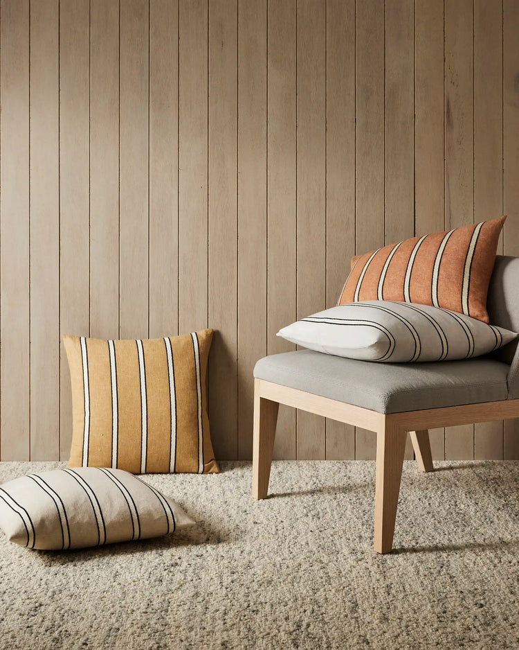 Warm minimalist bedroom with vertical shiplap walls, natural wood bed frame, and striped linen cushions in terracotta, cream, and neutral tones layered on white bedding and oatmeal rug.